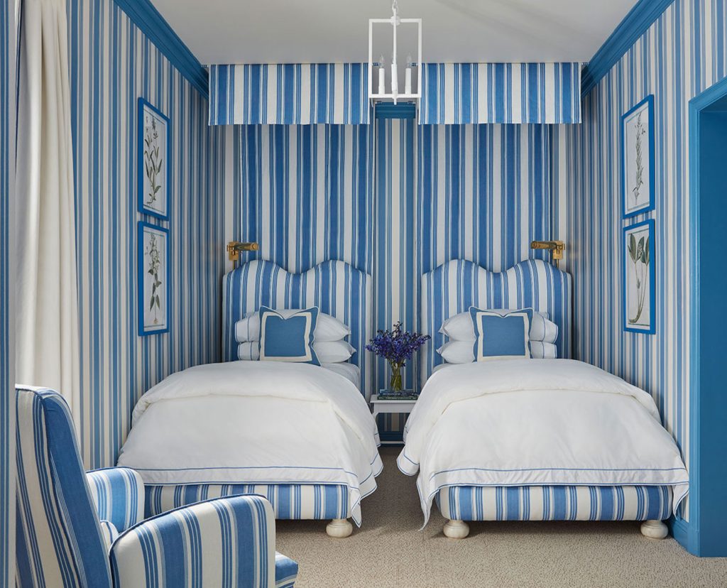 A cozy bedroom with blue and white striped wallpaper and two beds.