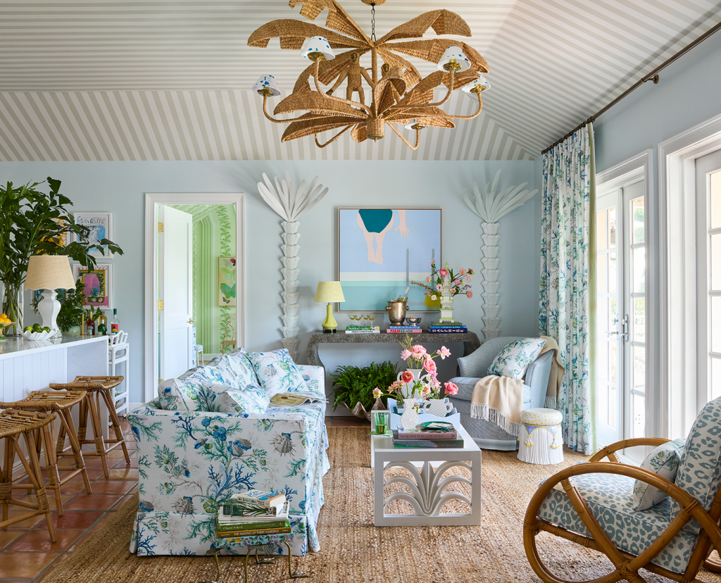 Villa living room with floral sofa, wicker chair, white coffee table, rattan chandelier, French doors, door leading to bedroom.